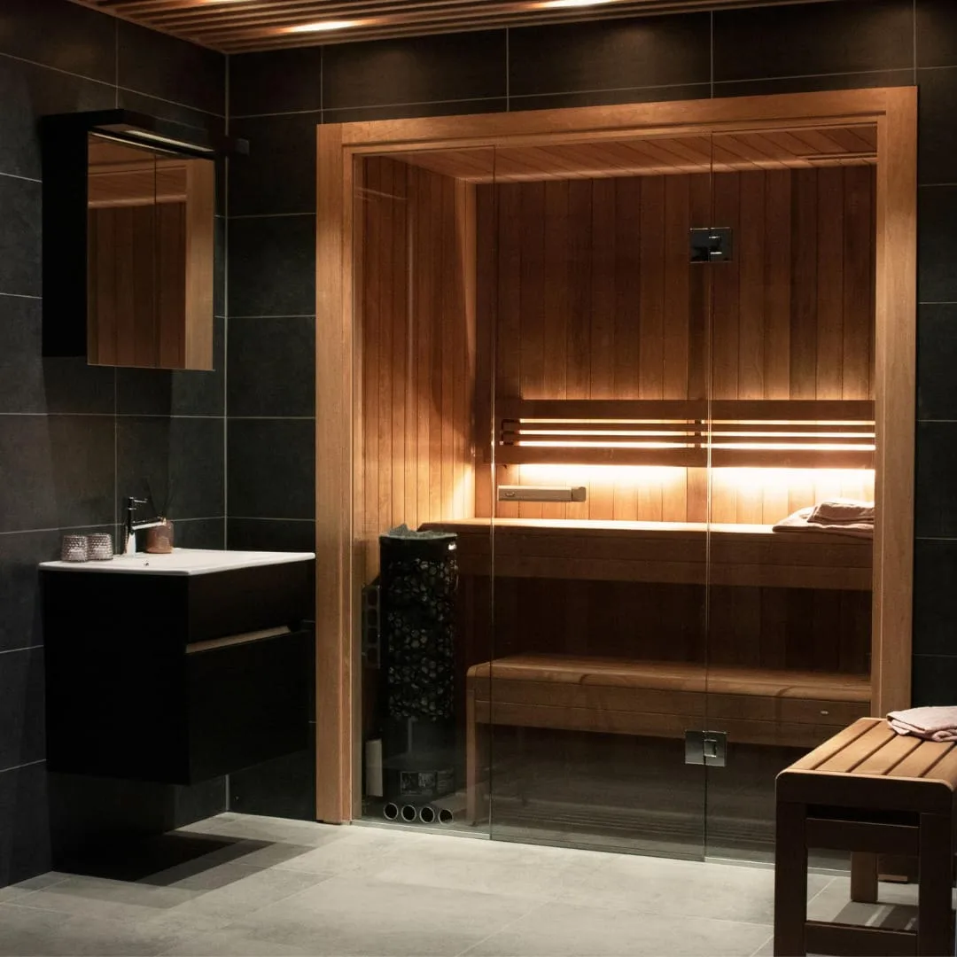 Tylö integrated indoor sauna with custom dark tile surrounds and frameless glass door, Roberts Leisure Isle of Man.