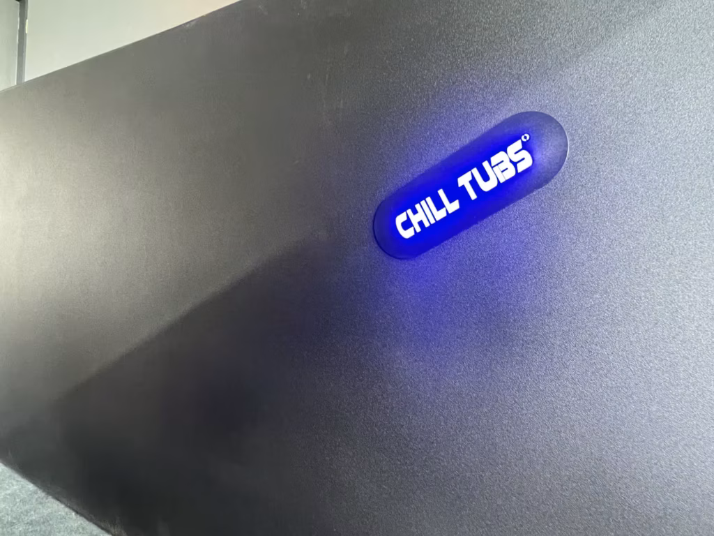 A close-up of the official Chill Tubs logo glowing with bright white text against a vibrant blue LED backlight on the dark textured exterior of the Chill Tub Lite.