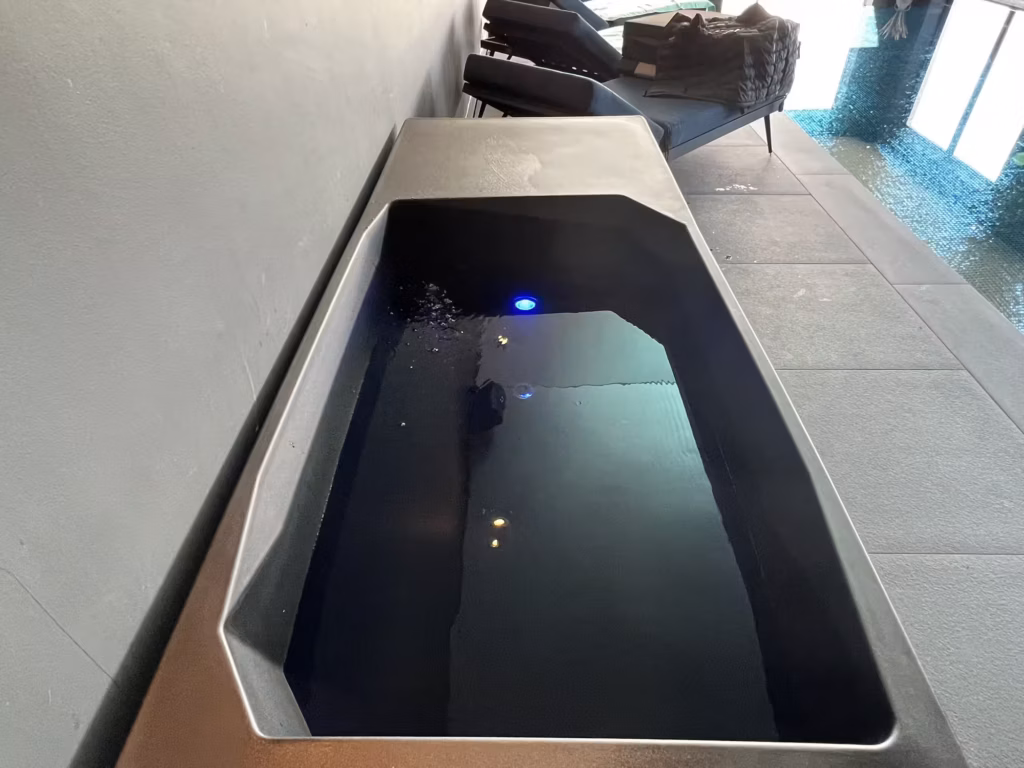 A top-down look into the water of a Chill Tub Lite cold plunge pool, showcasing its dark rotomolded interior, smooth safety rim, and a glowing blue underwater LED light.