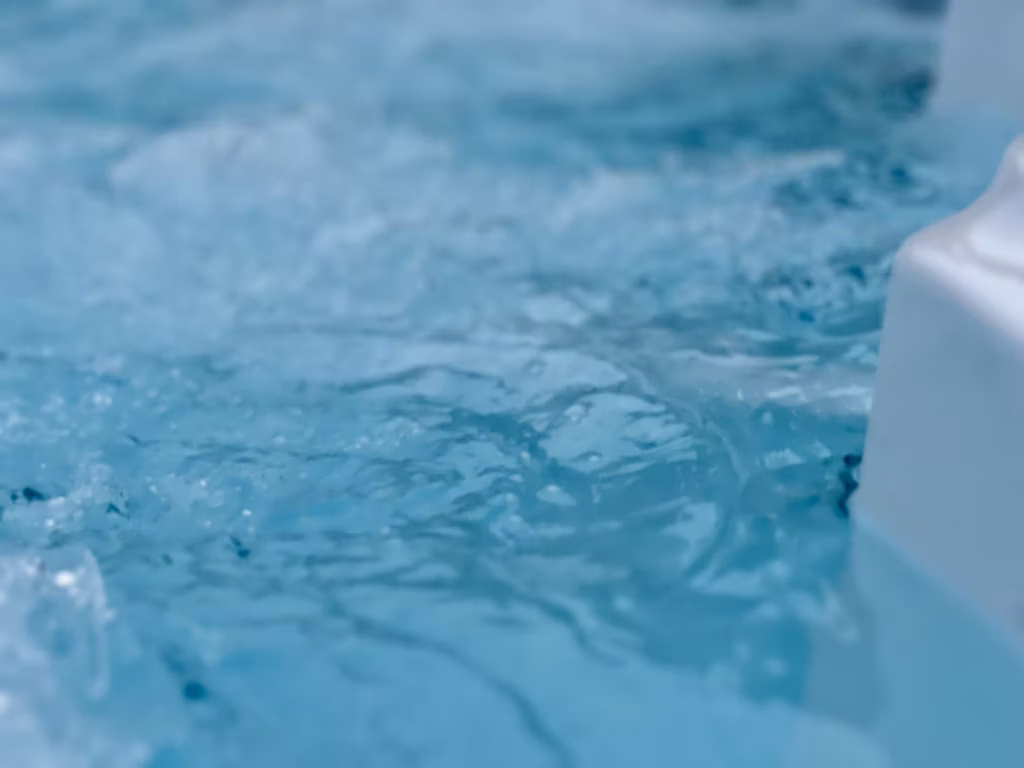 A macro close-up of churning, bright blue hydrotherapy water inside a luxury hot tub installed on the Isle of Man, showing a glimpse of the smooth white acrylic shell.