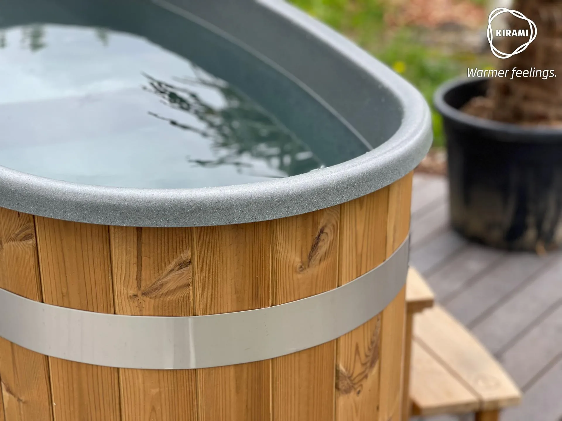 A close-up view detailing the premium light wood exterior paneling, stainless steel tension band, and smooth grey rim of a Kirami Original Tiny wood-fired hot tub on the Isle of Man.