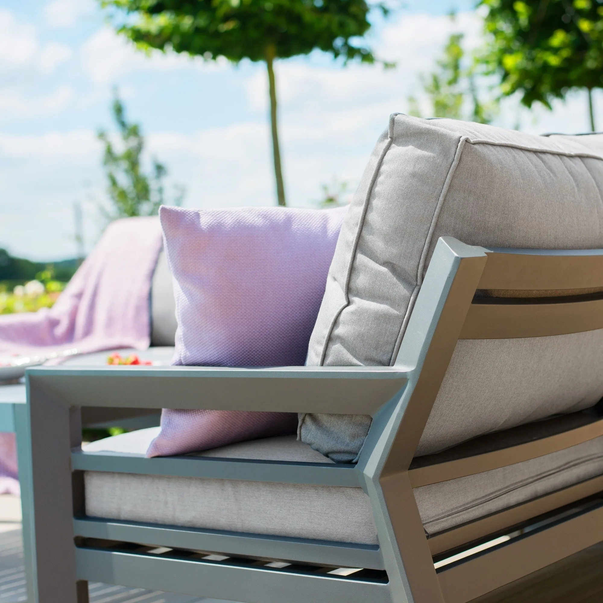 Close-up of the angular dark aluminium armrest and thick dove grey cushions on the Maze New York Corner Sofa Set, styled with a purple throw pillow.