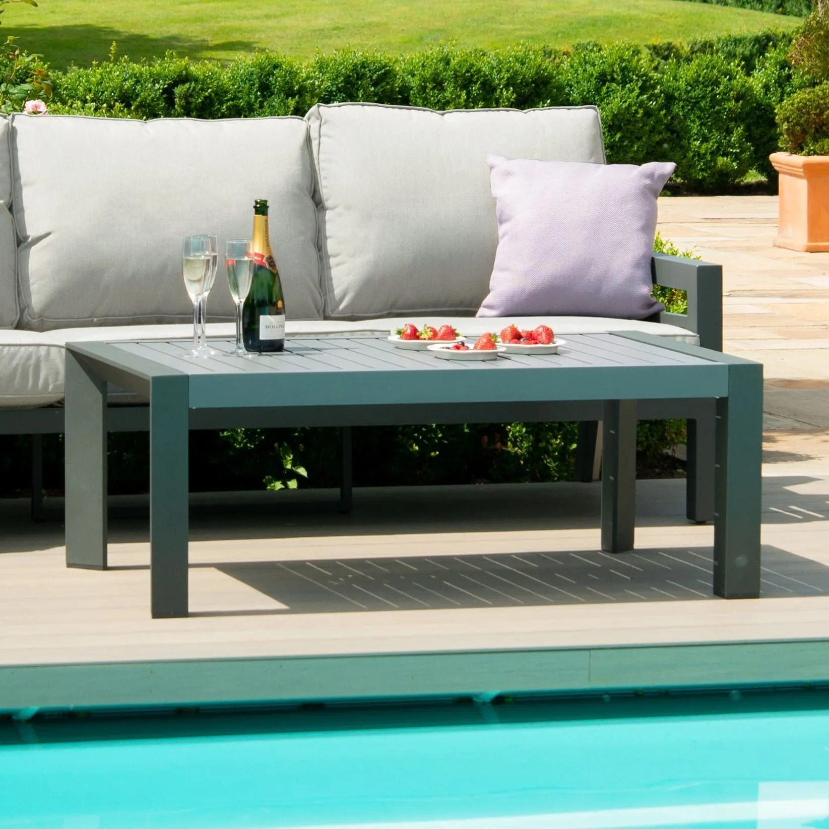 Dark aluminium slatted coffee table from the Maze New York Corner Sofa Set in Dove Grey, styled with champagne and strawberries by a pool.
