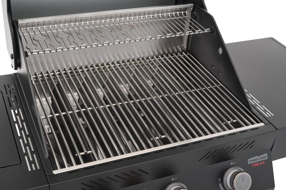 A detailed interior view of a Primeliner gas grill, featuring heavy-duty stainless steel cooking grates and an upper warming rack, with the "Prime Liner Ebull" branding visible on the side panel.