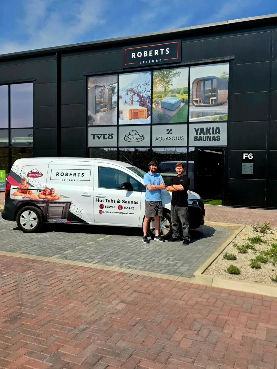 Exterior of the Roberts Leisure showroom on the Isle of Man, featuring two staff members next to a company van offering Arctic Spas, tylo Sauna, AquaSolos hot tubs and Yakia Saunas.