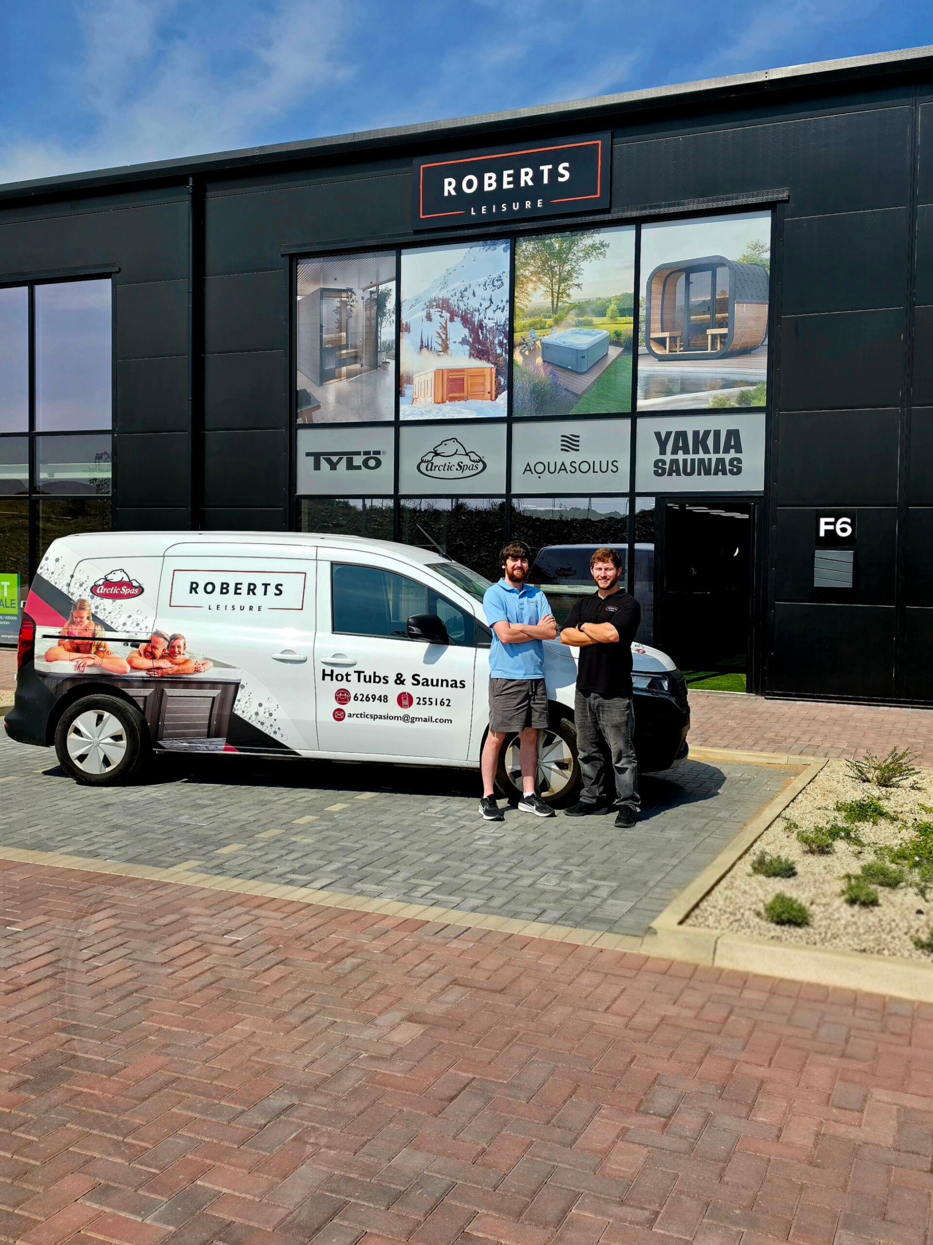 Exterior of the Roberts Leisure showroom on the Isle of Man, featuring two staff members next to a company van offering Arctic Spas, tylo Sauna, AquaSolos hot tubs and Yakia Saunas.