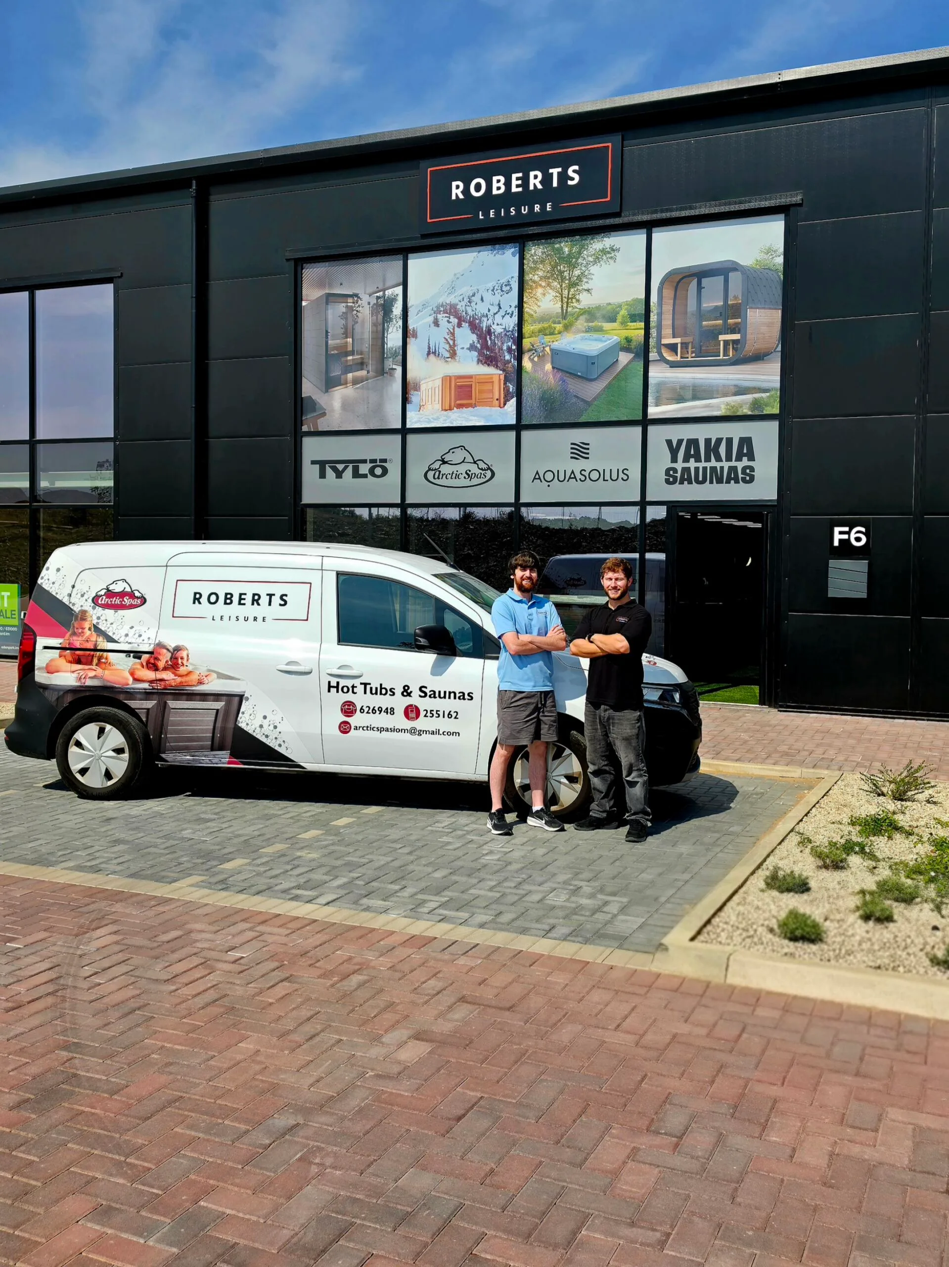 Exterior of the Roberts Leisure showroom on the Isle of Man, featuring two staff members next to a company van offering Arctic Spas, tylo Sauna, AquaSolos hot tubs and Yakia Saunas.