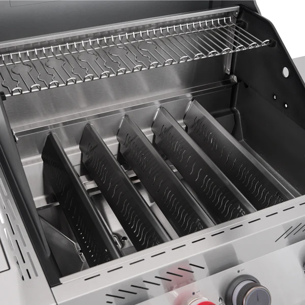An internal close-up view of the Primeliner S4 gas barbecue firebox with the main cooking grates removed, showcasing five angled stainless steel flame tamers and a wire warming rack.
