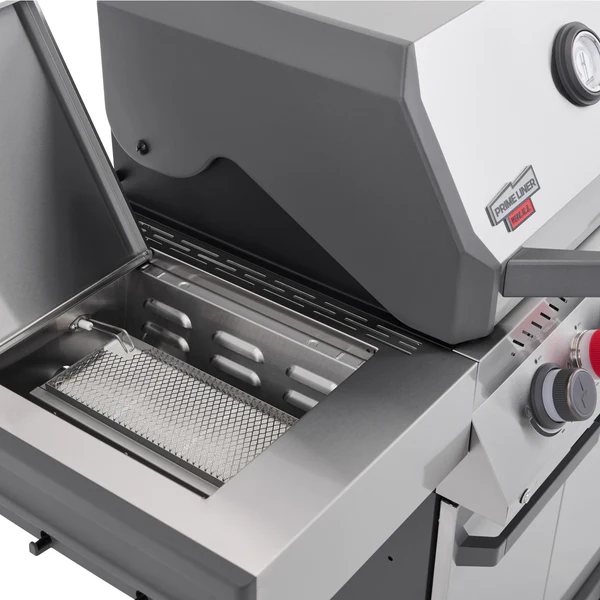 A close-up view of the Primeliner S4 gas grill's open side shelf revealing an integrated ceramic infrared sear burner next to the main stainless steel hood.