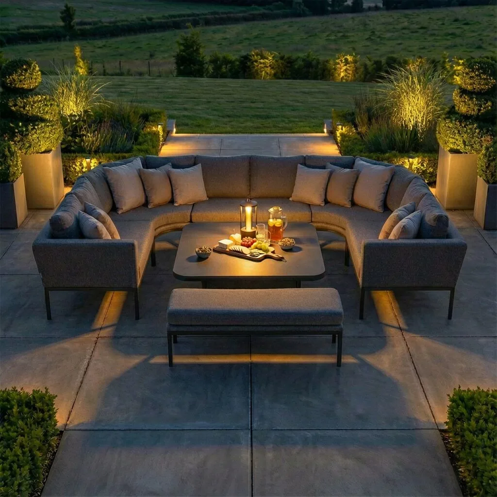 The Maze - Outdoor Fabric Pulse U Shape Corner Dining Set with Rising Table - Zinc Grey illuminated at night on a patio at Roberts Leisure in the Isle of Man.