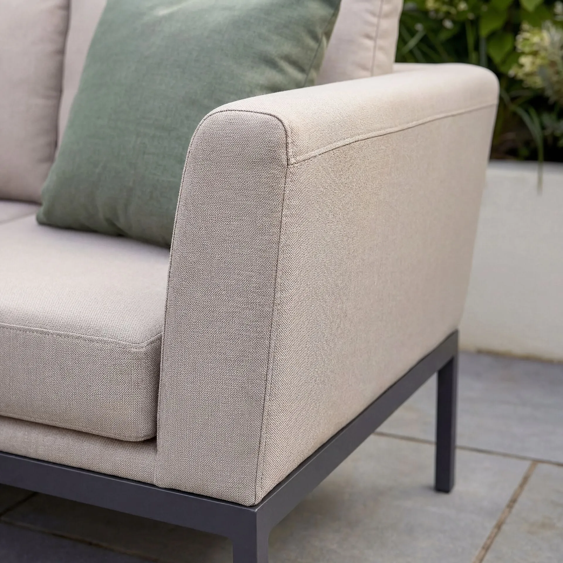 Close-up of the Maze Pulse sofa's side profile, showcasing the oatmeal all-weather fabric, a green throw pillow, and the sleek grey aluminium frame.