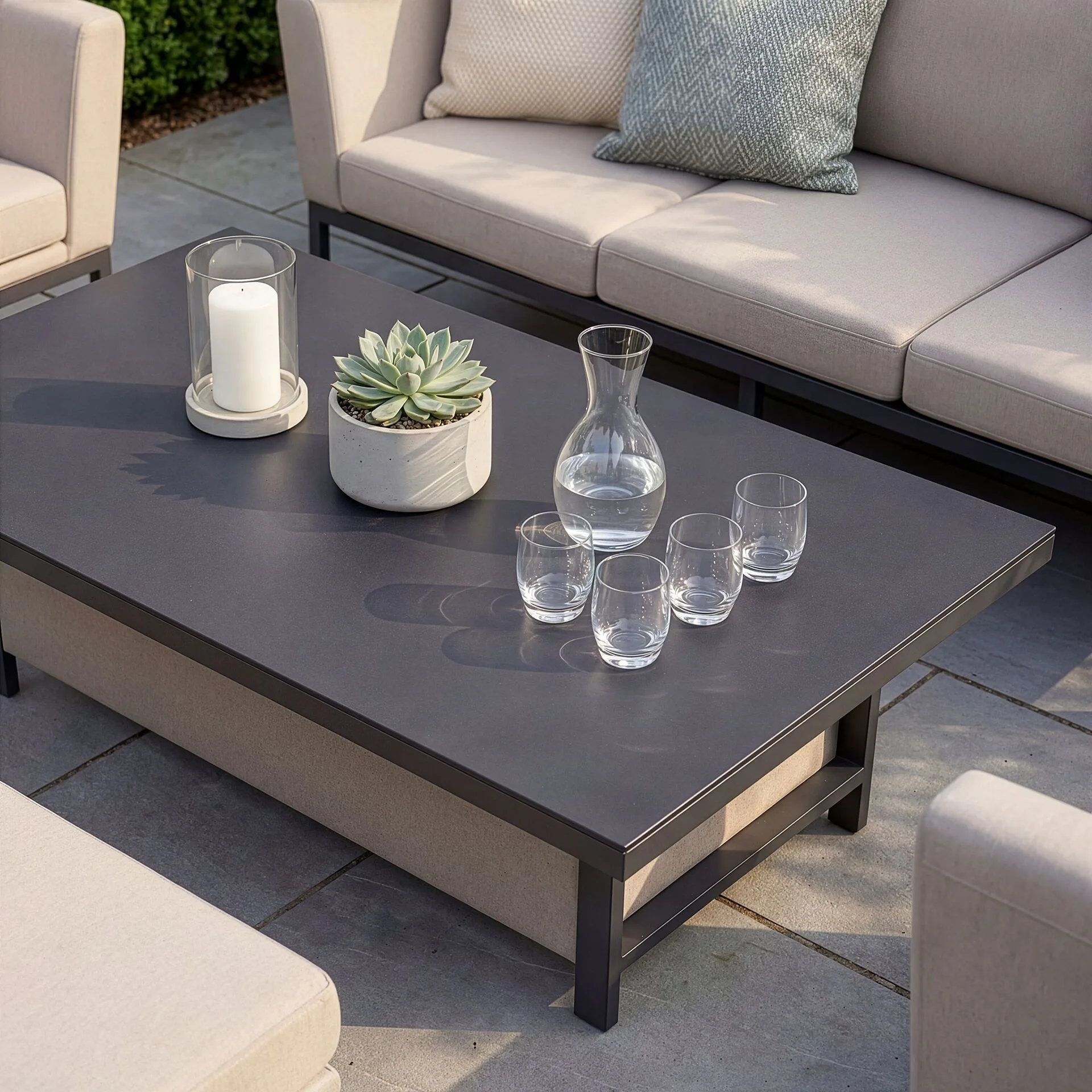 The Maze Pulse adjustable coffee table in its lowered position, set with drinks and a potted succulent, alongside the oatmeal fabric sofa.