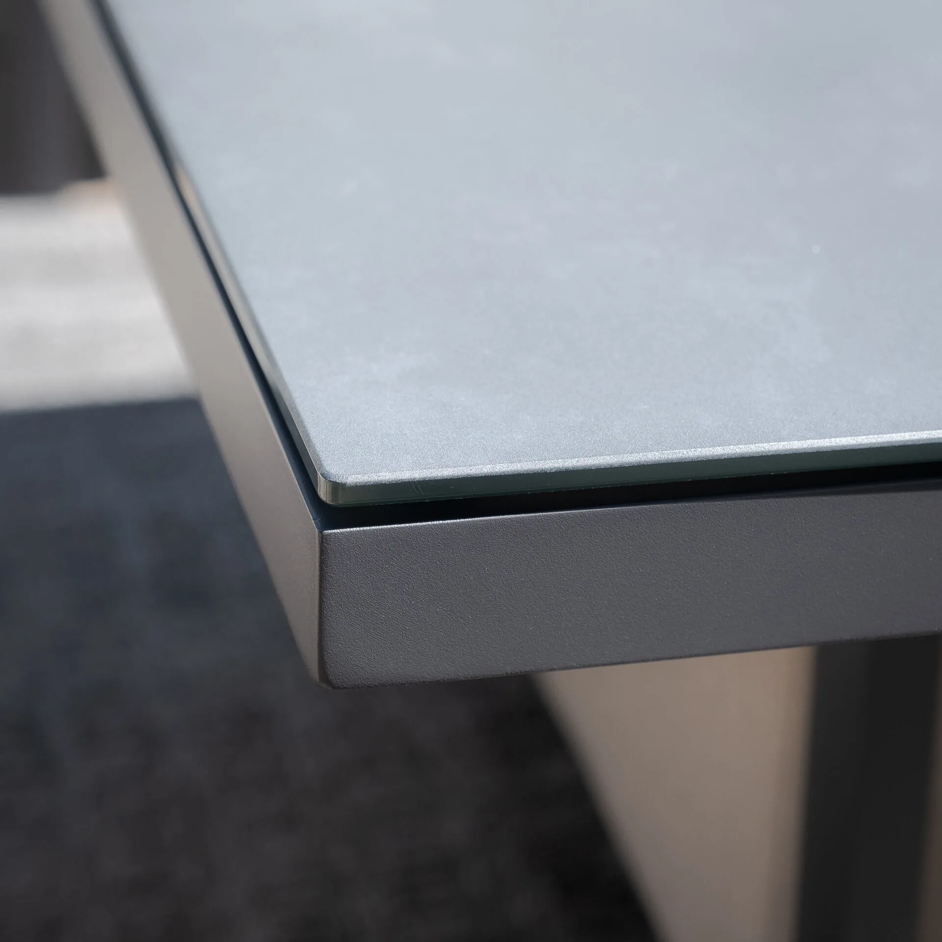 Close-up of the durable ceramic stone tempered glass table top and grey powder-coated aluminium frame on the Maze Pulse set.