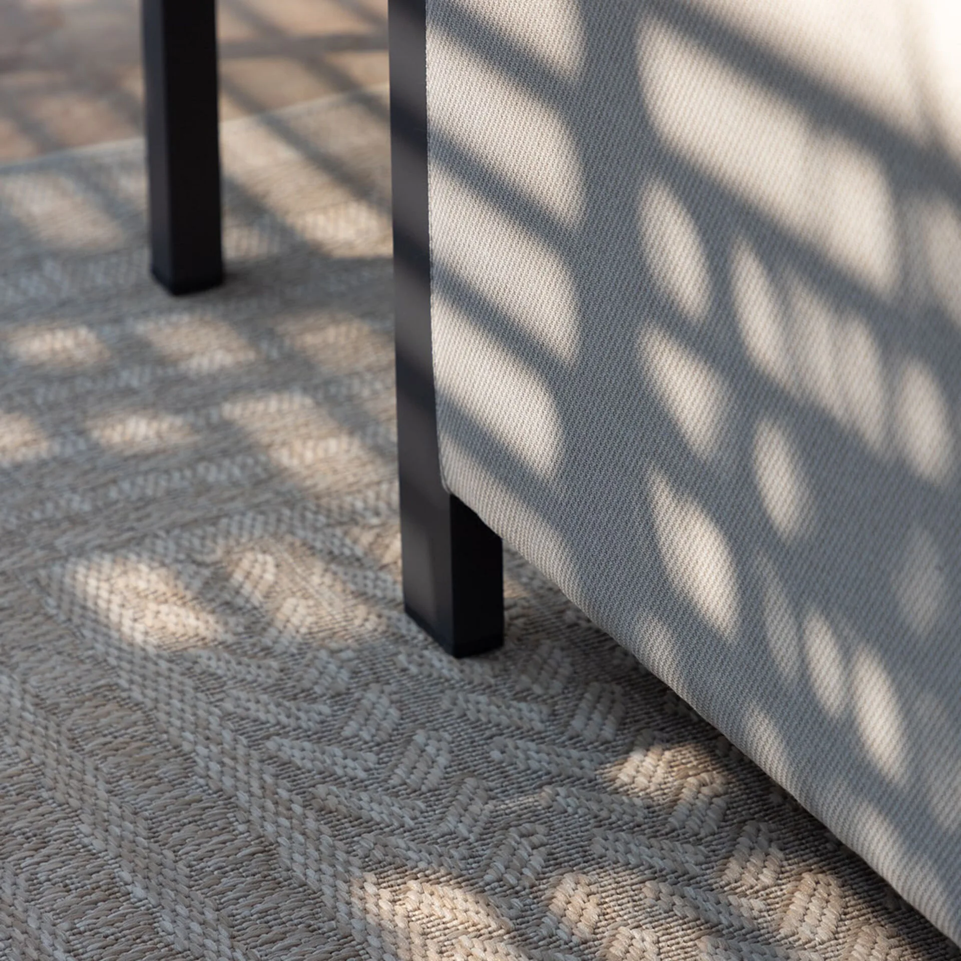 Close-up showing the robust grey powder-coated aluminium leg and mould-resistant Oatmeal fabric of the Maze Pulse garden sofa resting on a patio rug.