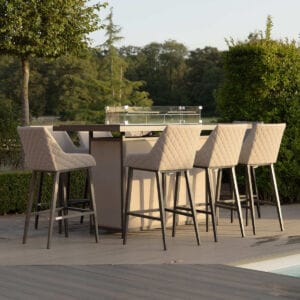 The Maze - Outdoor Fabric Regal 8 Seat Rectangular Bar Set Latte with café frame, featuring eight quilted high-rise stools and a ceramic glass table, located poolside at Roberts Leisure, Isle of Man.