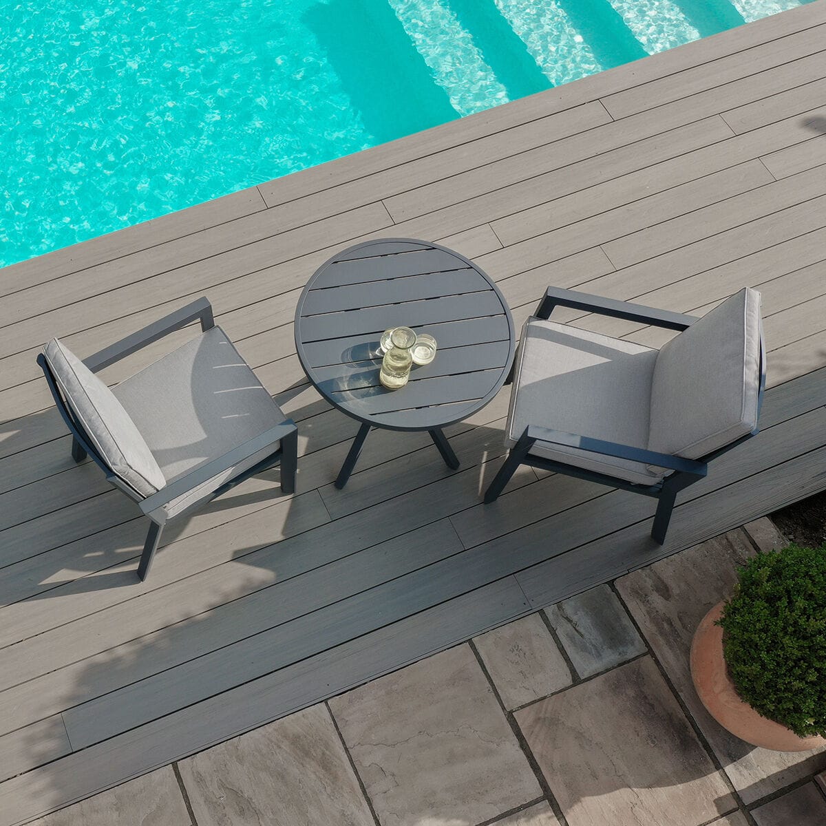 Top-down view of the Maze - New York 3 Piece Aluminium Bistro Set - Dove Grey featuring a slatted table and two chairs on a deck beside a pool at Roberts Leisure, Isle of Man.