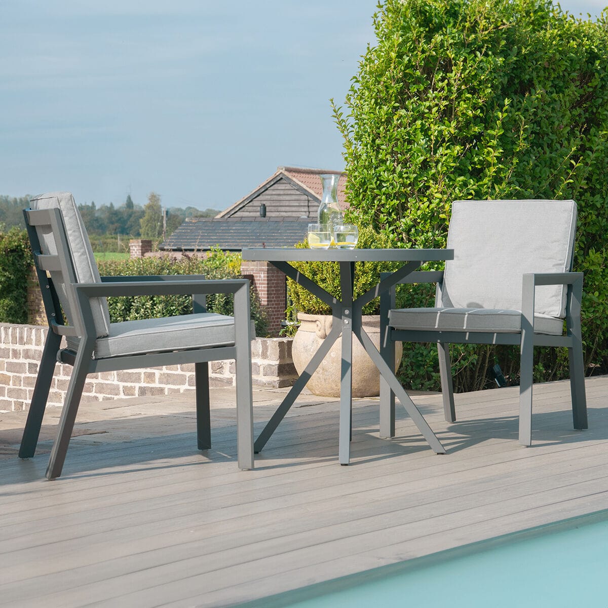 The Maze - New York 3 Piece Aluminium Bistro Set - Dove Grey with deep-filled polyurethane foam cushions, situated on a poolside deck at Roberts Leisure, Isle of Man.