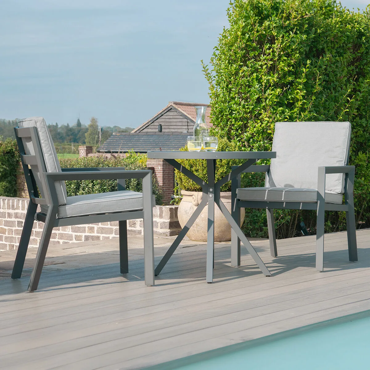 The Maze - New York 3 Piece Aluminium Bistro Set - Dove Grey with deep-filled polyurethane foam cushions, situated on a poolside deck at Roberts Leisure, Isle of Man.